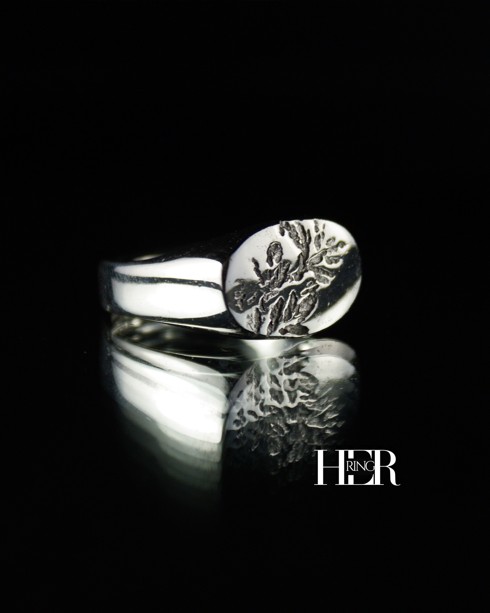 Srebrny sygnet damski, męski o podłużnym kształcie z widocznym odciskiem wrzosu, pokazany na czarnym tle.