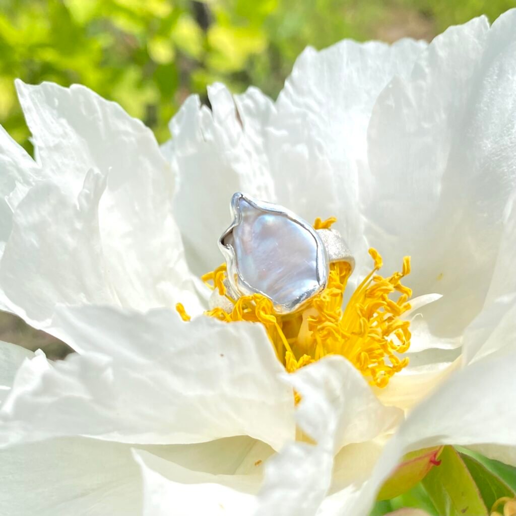 Srebrny sygnet damski z zakutą perłą hodowaną o nieregularnym kształcie, tło piwonia