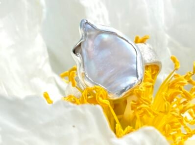 Srebrny sygnet damski z zakutą perłą hodowaną o nieregularnym kształcie, tło piwonia