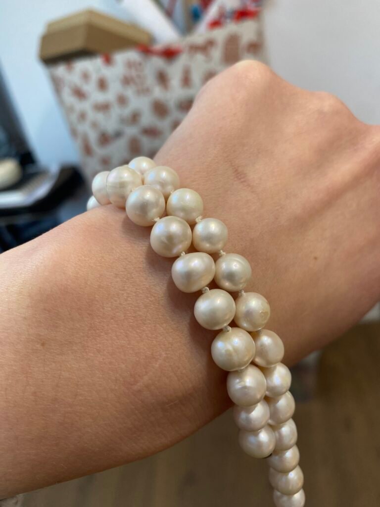 Skoro masz już gotowe, piękne sznury pereł po pętelkowaniu, zdjęcia powinny podkreślać tę rytmiczność supełków i precyzję wykonania. Klient musi poczuć, że to robota jubilerska, a nie zwykły sznurek.

Oto propozycje dla zdjęć prezentujących gotowe naszyjniki:

Zdjęcie 1: Zbliżenie (Makro) na supełki między perłami
To zdjęcie, na którym widać strukturę nici i precyzję węzłów.

Tekst alternatywny (ALT): Zbliżenie na profesjonalne pętelkowanie pereł na białej nici jedwabnej, widoczne precyzyjne supełki oddzielające perły.